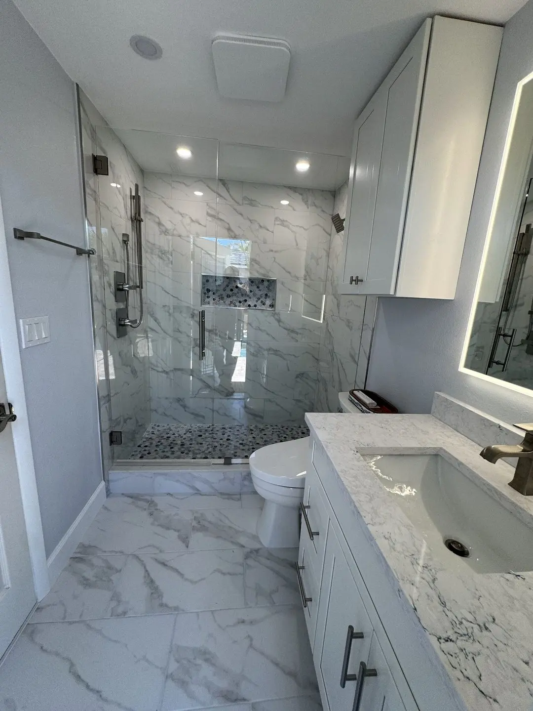 Walk in shower with marble look tile, a frameless glass door, a pebble mosaic floor, and a recessed niche in a remodeled St. Petersburg bathroom